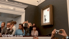 A Group Of People Are Taking Pictures Of A Painting Of A Girl With A Red Heart GIF