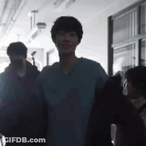 A Group Of People Are Walking Down A Hallway . GIF