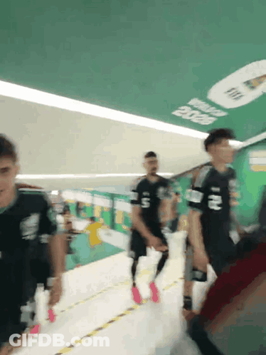 A Group Of People Are Walking Down A Hallway With A Sign On The Ceiling That Says Fifa 2020 GIF
