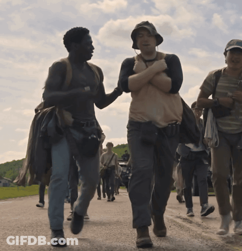 A Group Of People Are Walking Down A Road And One Man Is Holding Another Man 'S Arm GIF