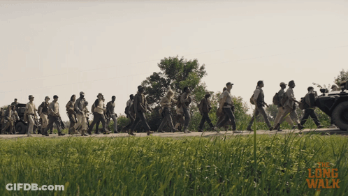 A Group Of People Are Walking Down A Road With The Words " The Long Walk " Written On The Bottom GIF