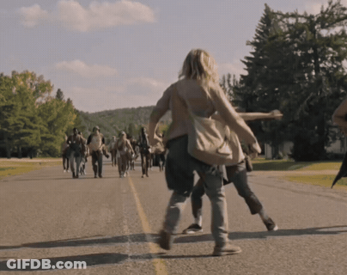 A Group Of People Are Walking Down A Road With Trees In The Background GIF
