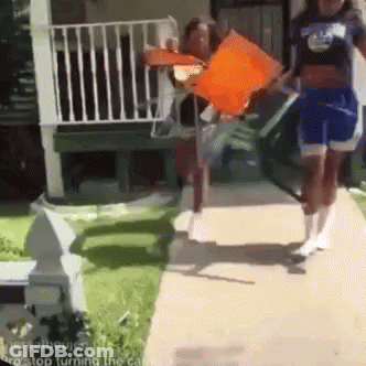 A Group Of People Are Walking Down A Sidewalk And One Of Them Is Holding An Orange Flag . GIF