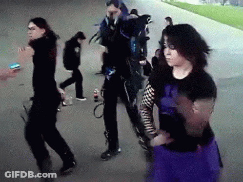 A Group Of People Are Walking Down A Sidewalk And One Of Them Is Wearing A Purple Skirt . GIF