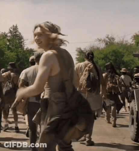 A Group Of People Are Walking Down A Street And A Woman Is Smiling In The Foreground GIF
