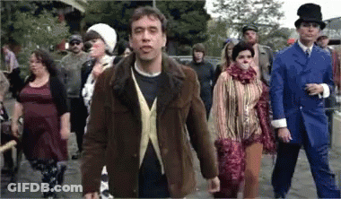 A Group Of People Are Walking Down A Street And One Man Is Wearing A Top Hat GIF