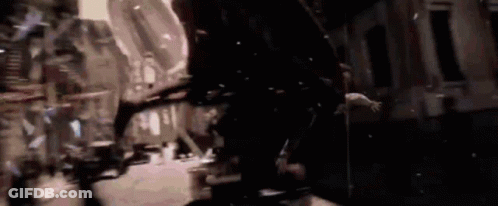 A Group Of People Are Walking Down A Street At Night In A Dark City . GIF