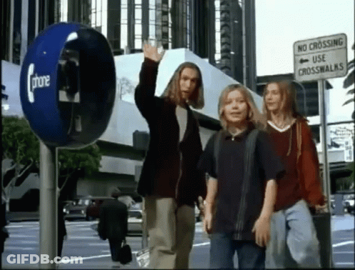 A Group Of People Are Walking Down A Street Next To A Phone Booth And A No Crossing Use Crosswalk Sign . GIF