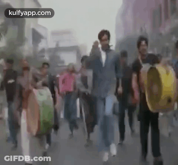 A Group Of People Are Walking Down A Street While Holding Drums . GIF
