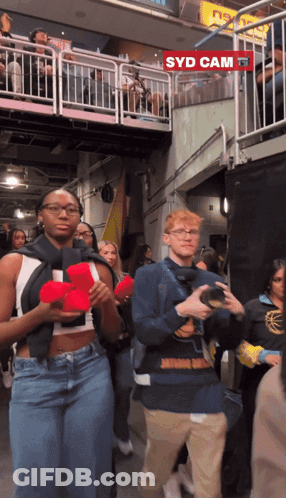 A Group Of People Are Walking In Front Of A Sign That Says Syd Cam GIF