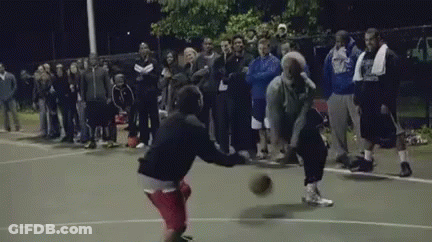 A Group Of People Are Watching Two Men Play Basketball On A Court At Night GIF
