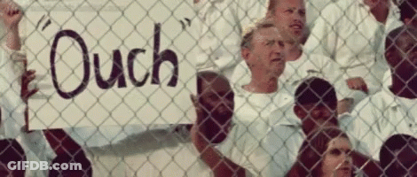 A Group Of People Behind A Chain Link Fence Holding A Sign That Says " Ouch " GIF