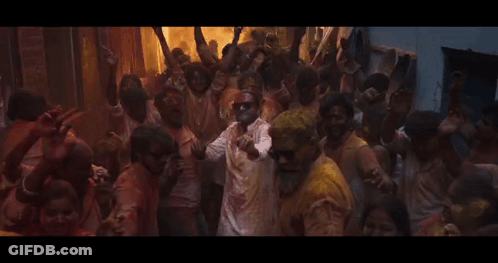 A Group Of People Covered In Colored Powder Are Dancing In A Room GIF