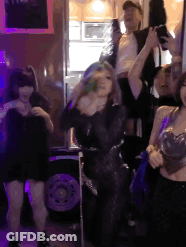 A Group Of People Dancing In A Dark Room With Purple Lights GIF