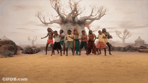 A Group Of People Dancing In Front Of A Tree In The Desert GIF
