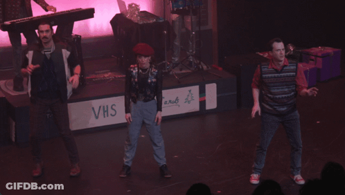 A Group Of People Dancing On A Stage With A Sign That Says Christmas Carols GIF