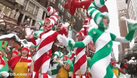 A Group Of People Dressed As Candy Canes Are Dancing In A Parade In A City . GIF