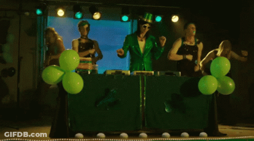 A Group Of People Dressed In Green Are Dancing In Front Of Green Balloons On A Stage GIF