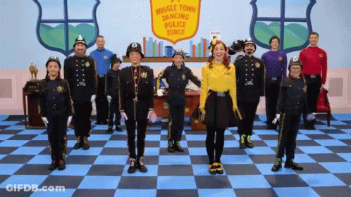 A Group Of People Dressed In Police Uniforms Are Standing In Front Of A Sign That Says Muggle Town Dancing Police Force GIF