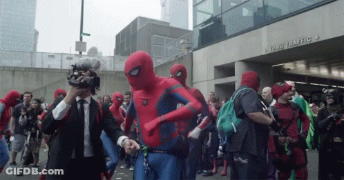 A Group Of People Dressed In Spiderman Costumes Are Walking Down A Street In Front Of A Building That Says Thru Traffic GIF