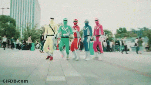 A Group Of People Dressed In Superhero Costumes Are Walking Down A Sidewalk . GIF
