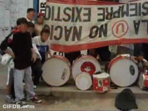 A Group Of People Holding Drums In Front Of A Banner That Says Siempre Existe GIF