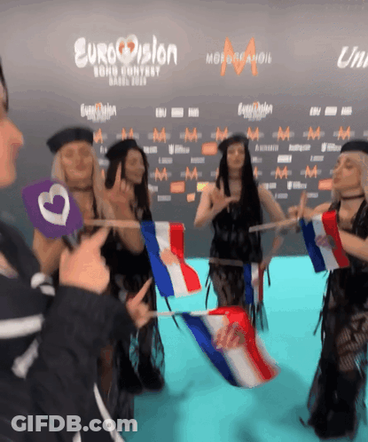 A Group Of People Holding Flags In Front Of A Eurovision Sign GIF