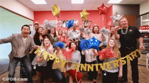 A Group Of People Holding Up Balloons And A Banner That Says Happy Anniversary GIF