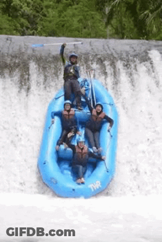 A Group Of People In A Blue Raft Are Standing On Top Of A Waterfall . GIF