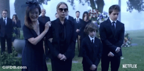 A Group Of People In Black Suits Are Standing In Front Of A Grave . GIF