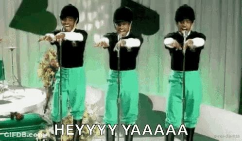A Group Of People In Green Pants And Black Shirts Are Standing In Front Of Microphones And Singing . GIF