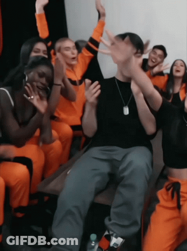 A Group Of People In Orange Jumpsuits Are Sitting Around A Table GIF