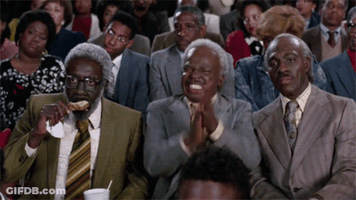 A Group Of People In Suits And Ties Are Sitting In A Theatre Applauding GIF