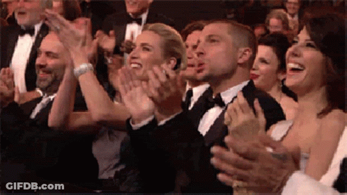 A Group Of People In Tuxedos Are Clapping Their Hands In A Crowd . GIF