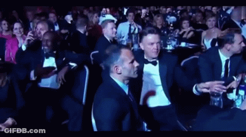 A Group Of People In Tuxedos Are Sitting In A Dark Room GIF
