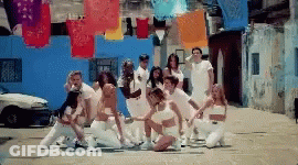 A Group Of People In White Clothes Are Dancing In Front Of A Blue Building GIF