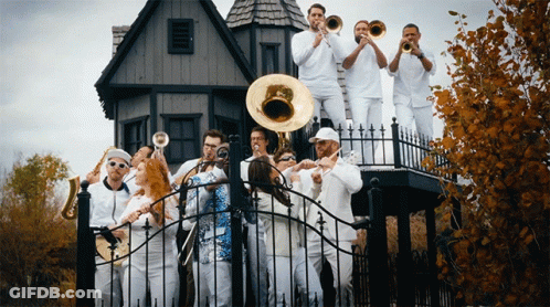 A Group Of People In White Playing Instruments In Front Of A House GIF
