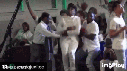 A Group Of People In White Shirts Are Dancing In A Room With A Green Light Behind Them . GIF
