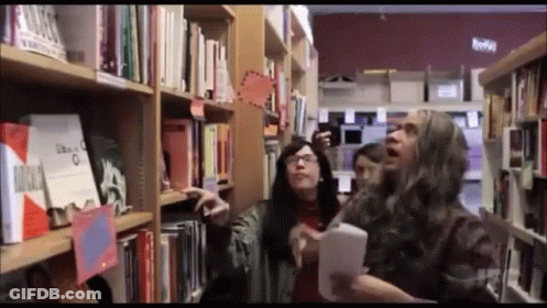 A Group Of People Looking At Books In A Library With A Sign That Says " Libros " GIF