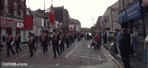 A Group Of People March Down A Street In Front Of A Kfc GIF