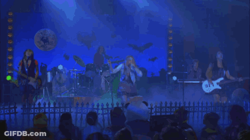 A Group Of People Playing Instruments On A Stage In Front Of A Sign That Says Gdg GIF