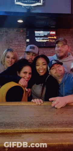 A Group Of People Posing For A Picture In Front Of A Sign That Says Dark Lager On It GIF