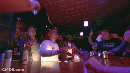 A Group Of People Raising Their Arms In The Air In A Bar GIF