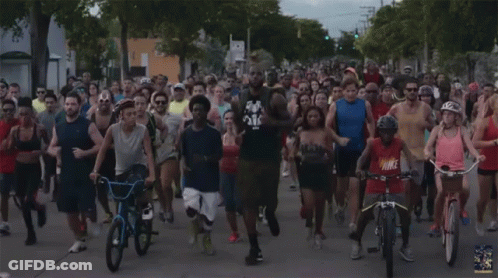 A Group Of People Running And Riding Bicycles With One Wearing A Red Shirt That Says Nike GIF