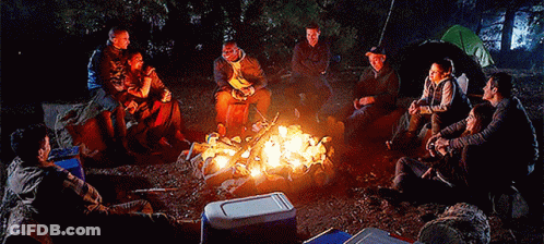A Group Of People Sitting Around A Campfire With A Blue Cooler In The Foreground GIF