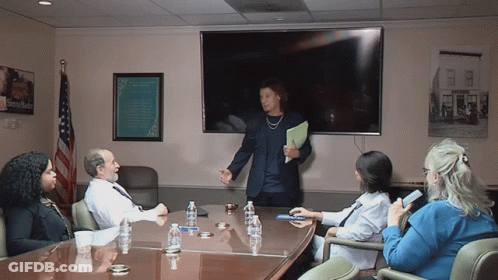 A Group Of People Sitting Around A Conference Table With A Sign On The Wall That Says ' Sidney Smith ' GIF