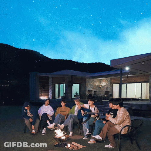 A Group Of People Sitting Around A Fire With One Wearing A Sweatshirt That Says ' Abercrombie ' On It GIF