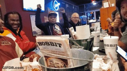 A Group Of People Sitting Around A Table With A Sign That Says Hobbit On It GIF