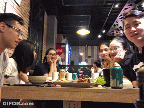 A Group Of People Sitting At A Table In Front Of A Coca Cola Fridge GIF