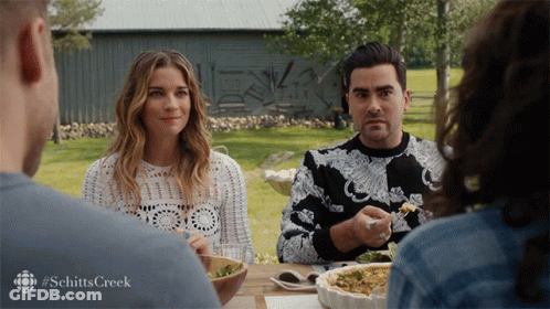 A Group Of People Sitting At A Table With The Word Schitts Creek On The Bottom Right GIF